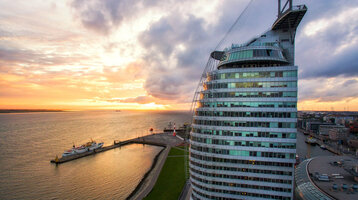 ATLANTIC Hotel Sail City – Außenansicht ATLANTIC Hotel Sail City in Bremerhaven, bei Sonnenuntergang am Wasser, mit modernem, gebogenem Glasdesign.