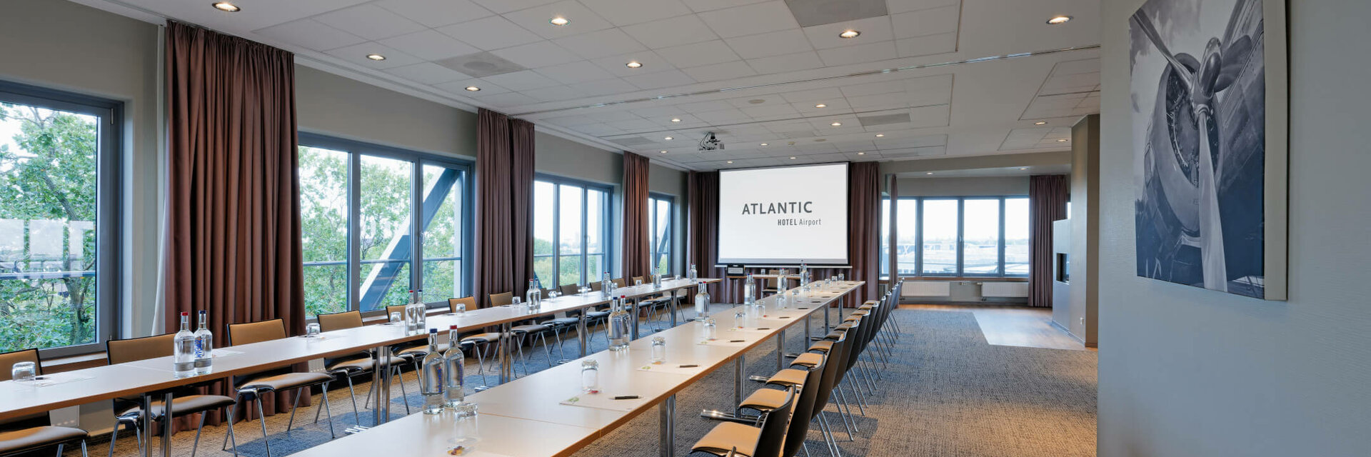 ATLANTIC Hotel Airport U-Form Tagungsraum Heller Konferenzraum mit U-förmiger Bestuhlung, großen Fenstern und Projektionsleinwand im ATLANTIC Hotel Airport Bremen.