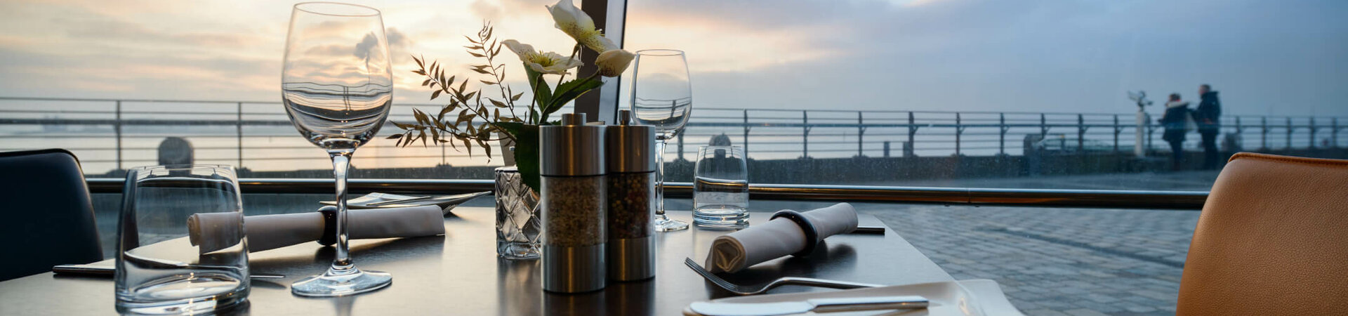 ATLANTIC Hotel SAIL CITY Restaurant STROM Gedeckter Tisch mit Blumen und Sonnenuntergangsblick im ATLANTIC Hotel Sail City, Bremerhaven.