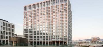 Modernes Hochhaus des ATLANTIC Hotel Heidelberg bei Sonnenuntergang, mit Glasfassade und umliegendem Platz.