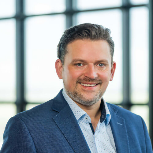 Director of Sales Bremen/Lower Saxony Man in blue suit smiling in front of window at ATLANTIC Hotel Airport Bremen.