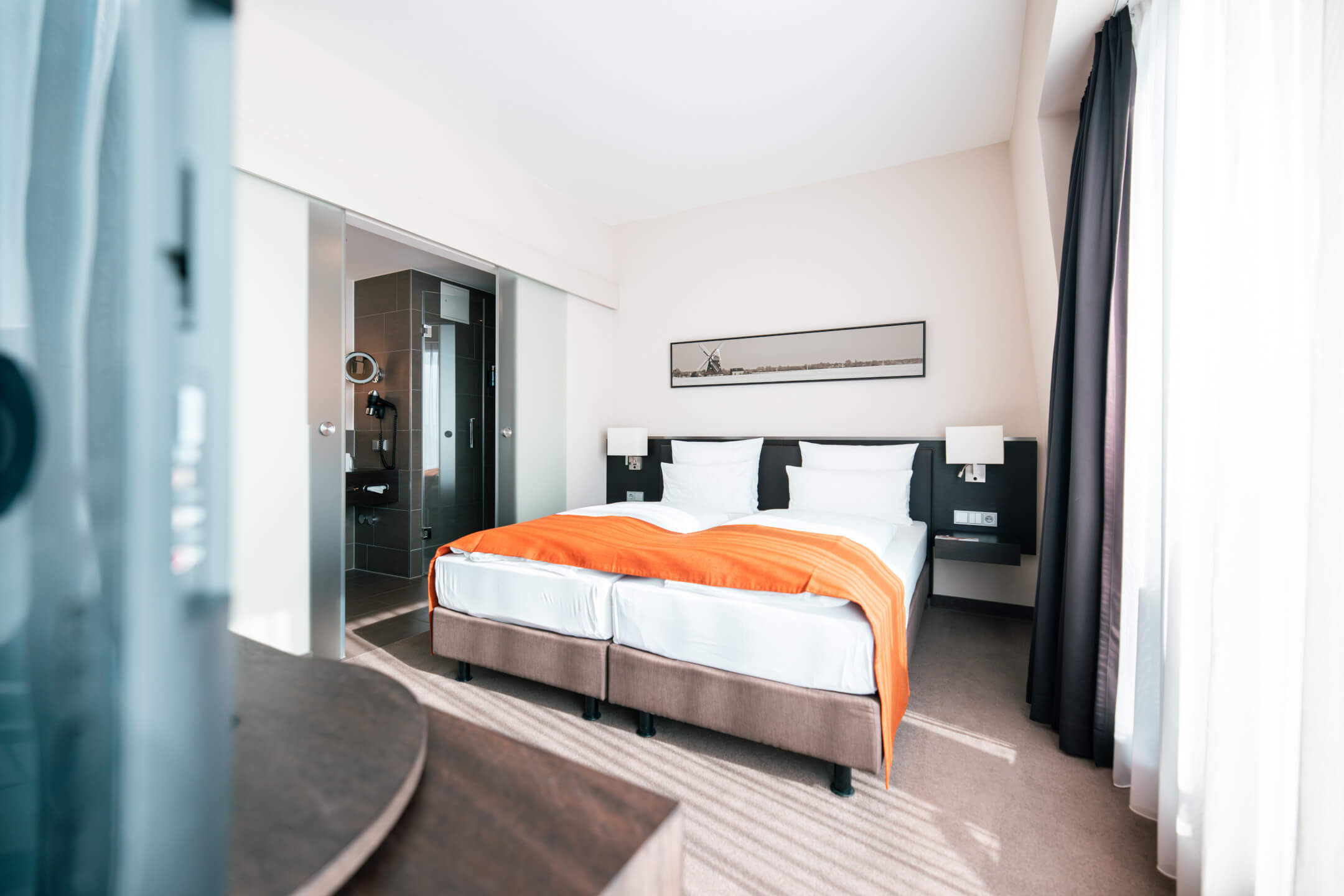 ATLANTIC Hotel Lübeck Studio Bright hotel room with double bed, orange ceiling, modern bathroom and large window at the ATLANTIC Hotel Lübeck.