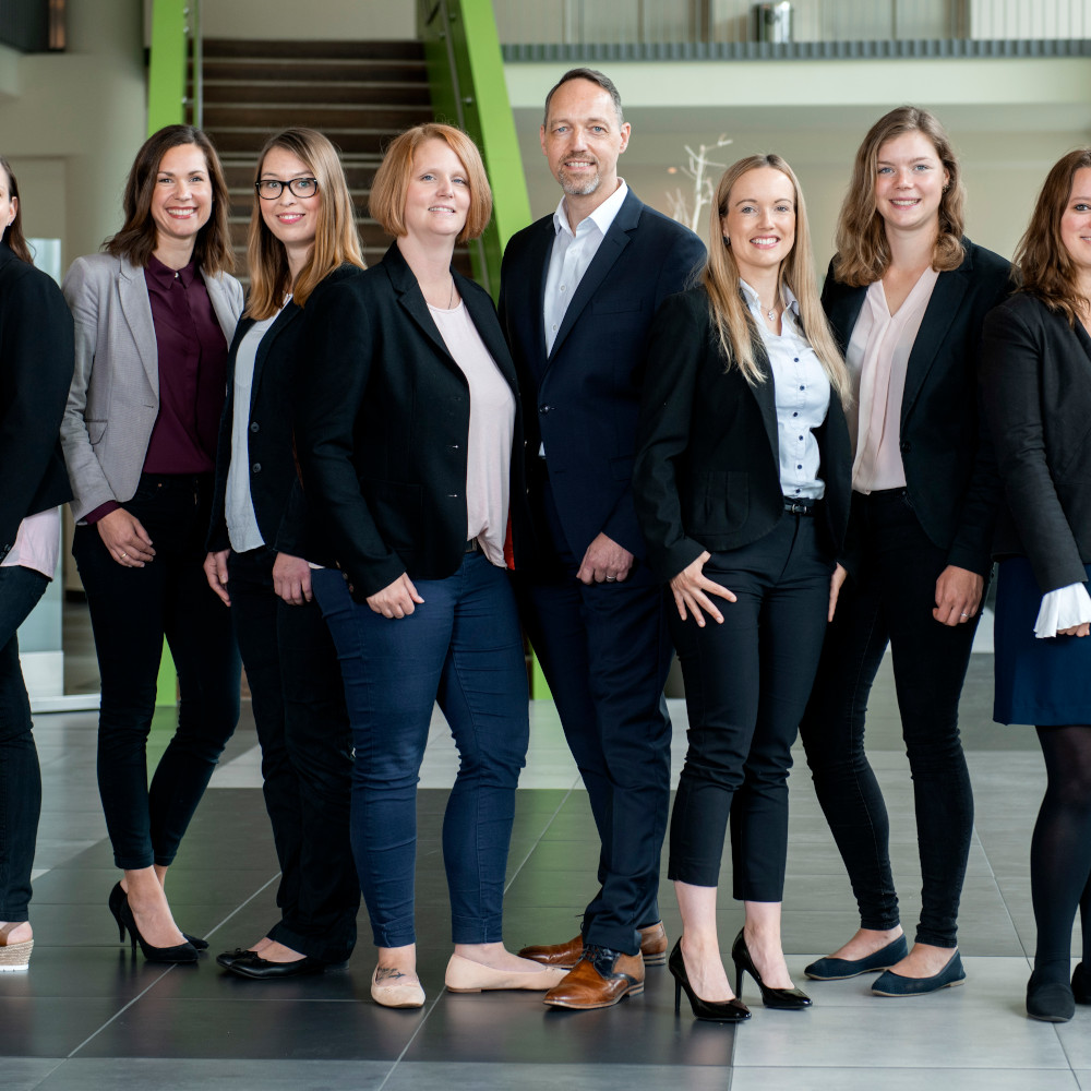 A group of hotel employees in business attire stand smiling in the lobby of the ATLANTIC Hotel Sail City.