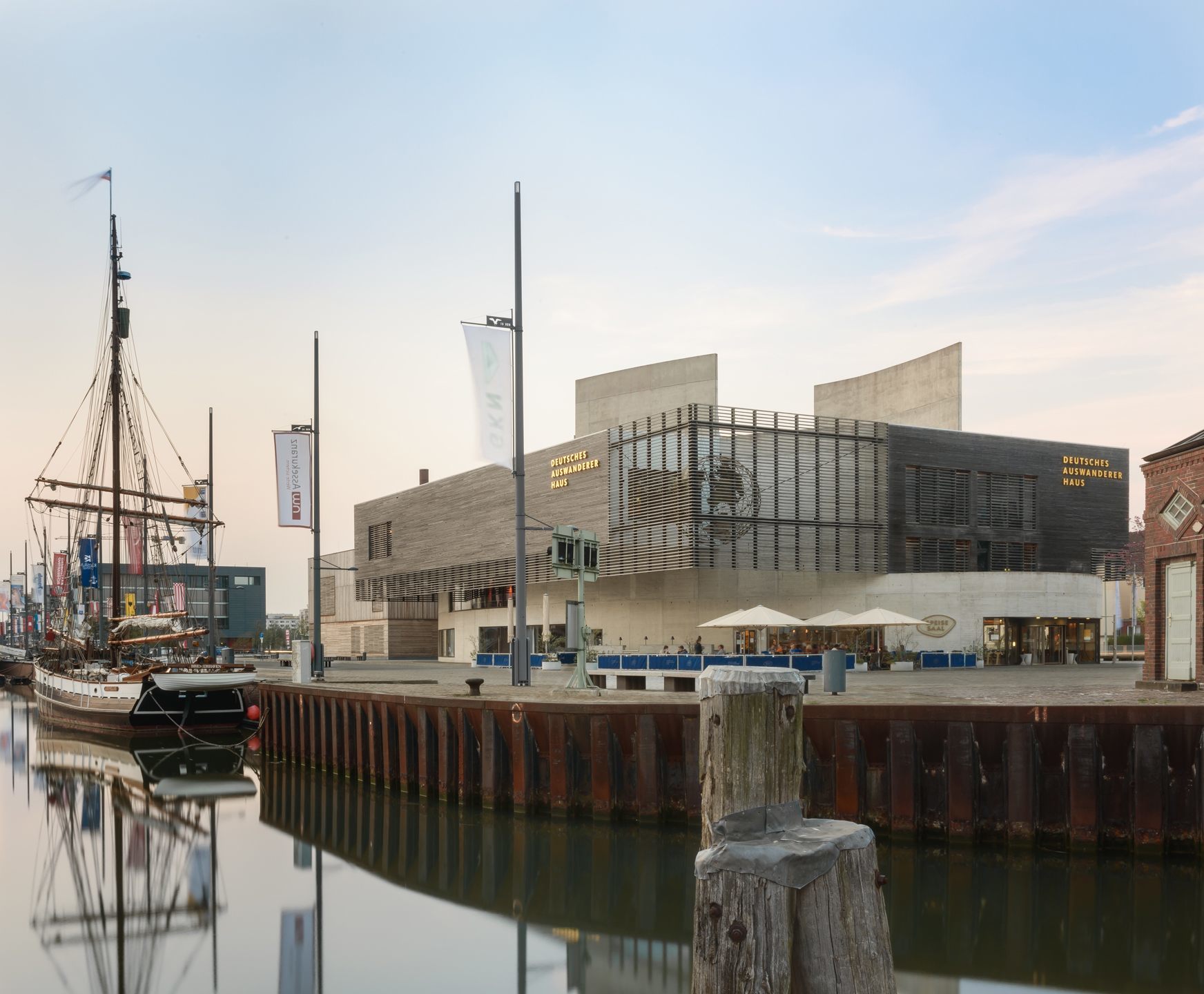 Exterior view of the German Emigration Centre in Bremerhaven Modern buildings at the harbor with sailing ship and promenade; German Emigration Center in the background.