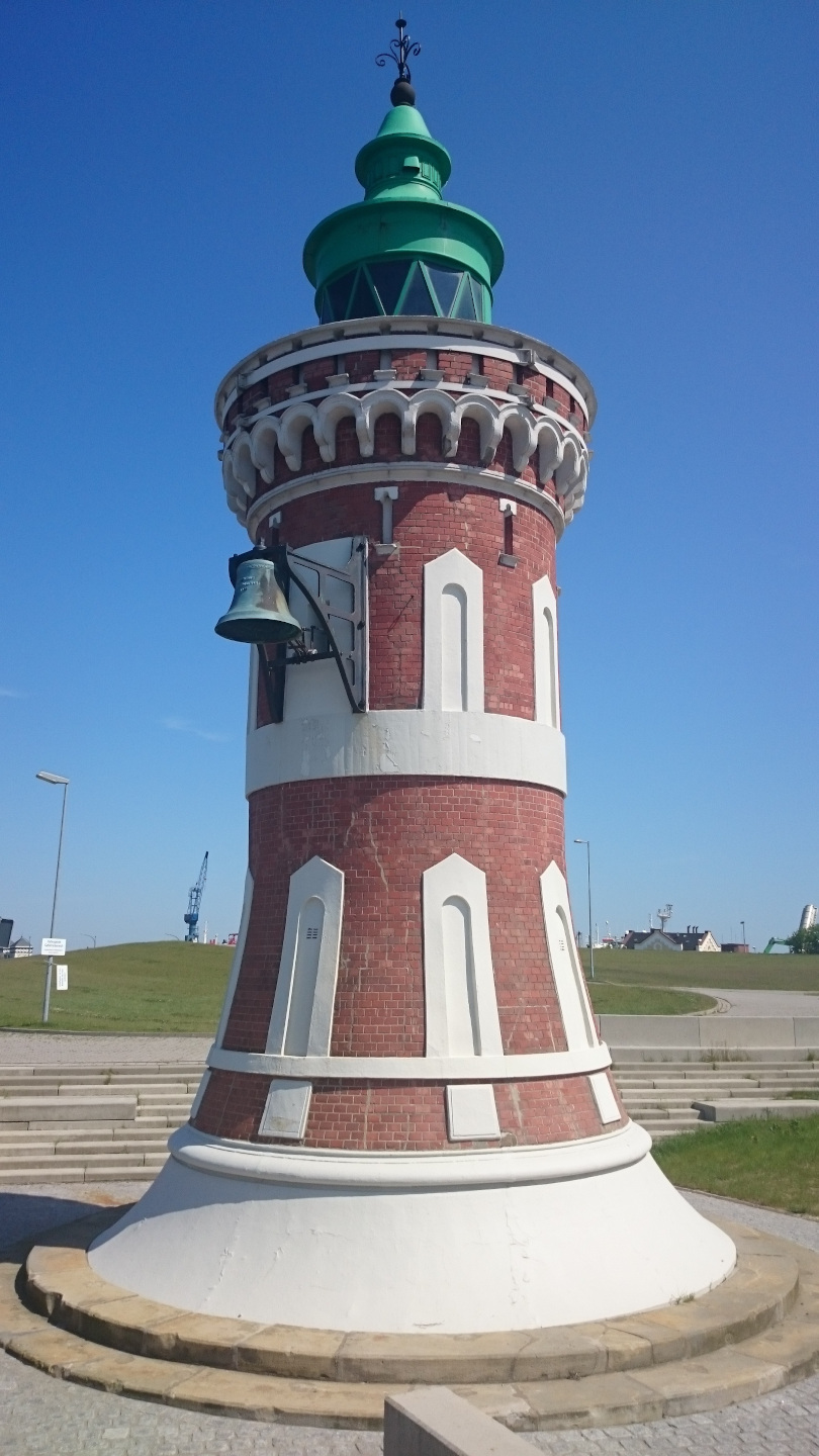 The Pingelturm in Bremerhaven | ATLANTIC Hotel Sail City Round lighthouse made of red brick with a green roof and bell, set against a blue sky.