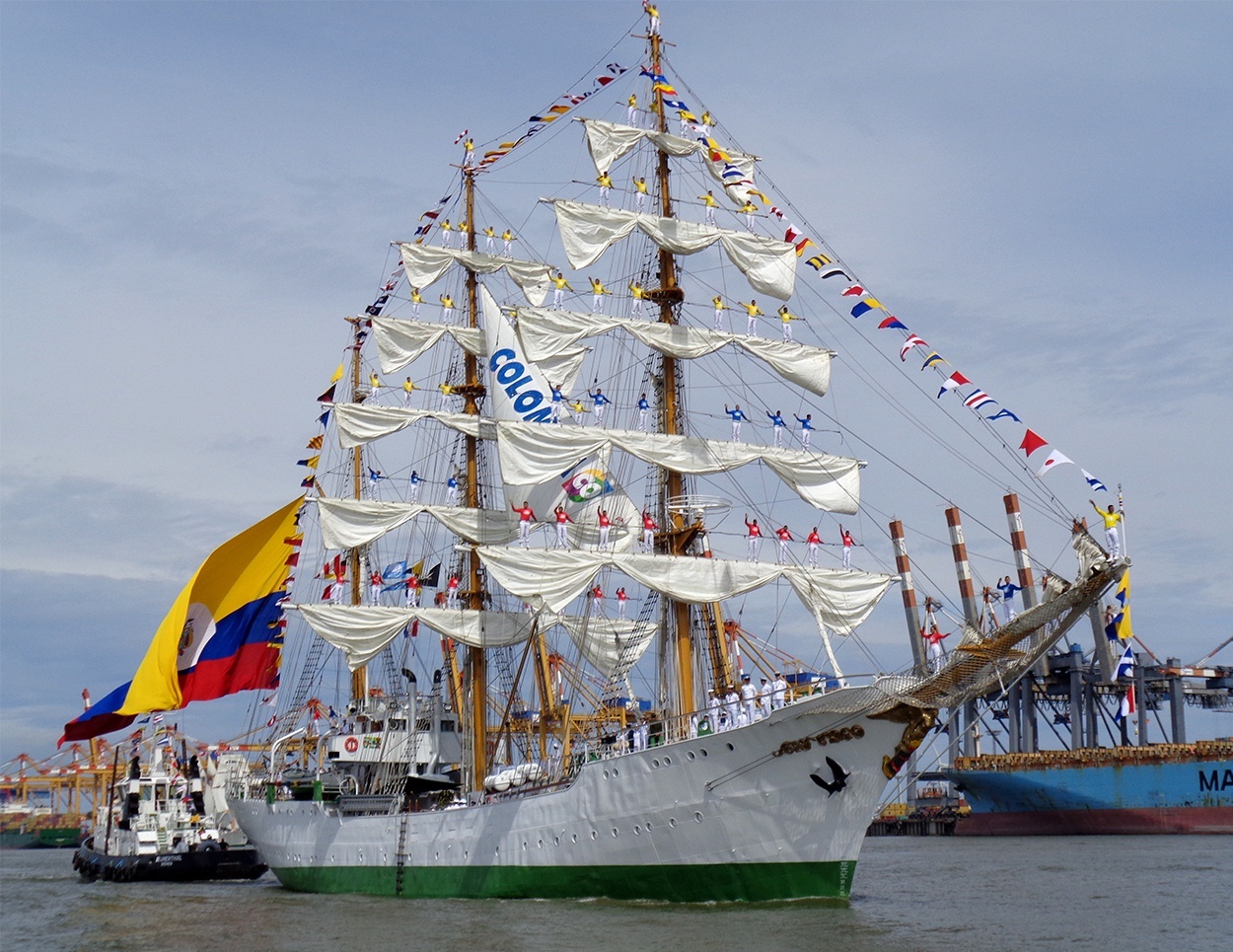 Large sailing ship with white sails, Colombian flag and colorful pennants in the harbor.