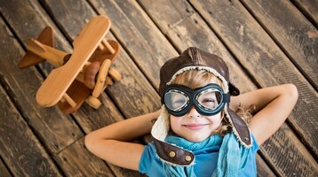 Child in the ATLANTIC Hotel Airport in Bremen Child with aviator cap and glasses lies smiling on wooden floor next to wooden airplane.