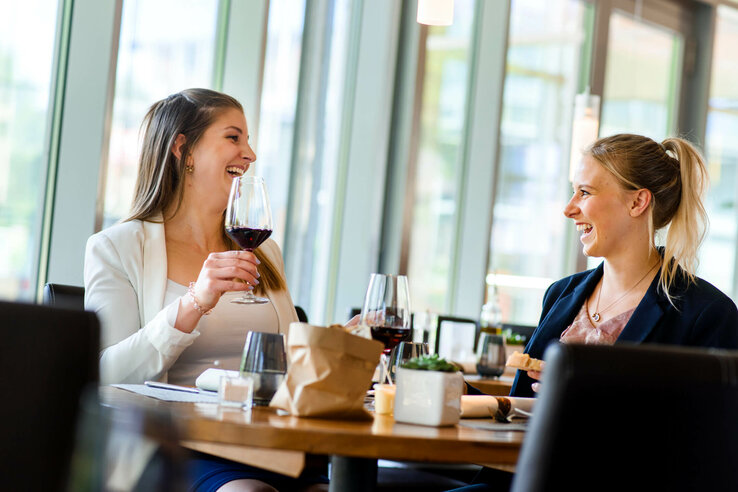 Guests in the Restaurant| Restaurant CAMPUS im ATLANTIC Hotel Universum Two women laugh and enjoy a glass of red wine in a bright restaurant at the ATLANTIC Hotel Universum.