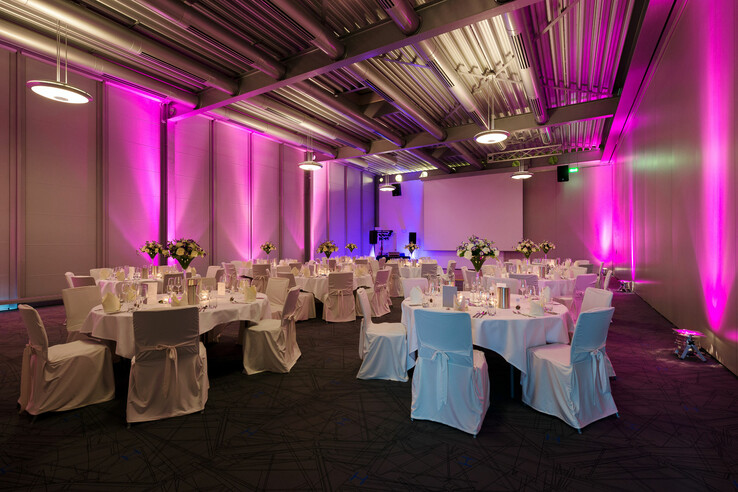 SMART events – Function rooms for your private parties or business events Modern banquet hall in the ATLANTIC Hotel Universum, Bremen, with round tables, white chairs and pink lighting.