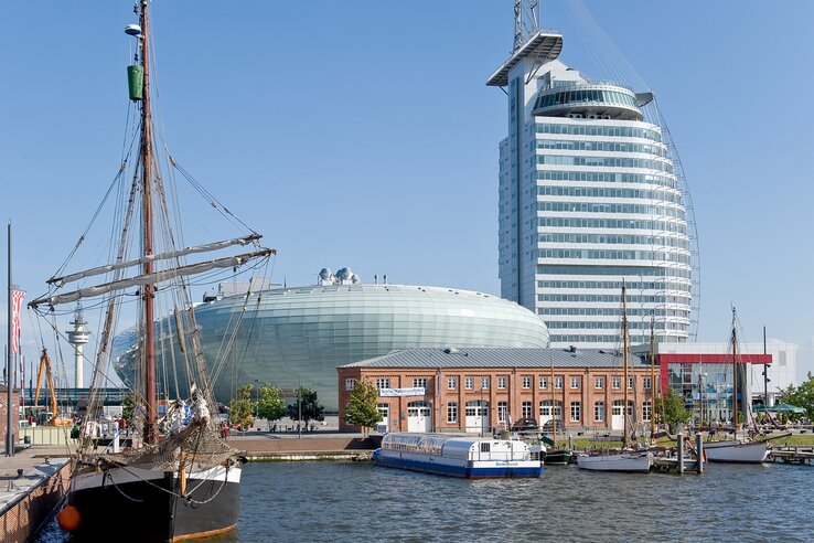 Exterior view of the ATLANTIC Hotel Sail City Bremerhaven Harbor view with sailing ship, modern glass building and historic brick building under a clear sky.