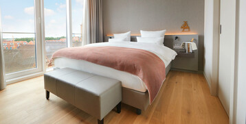 Balcony Suite sleeping area at the Atlantic Grand Hotel Bremen Bright hotel room with large bed, floor-to-ceiling windows and city view at the ATLANTIC Grand Hotel Bremen.
