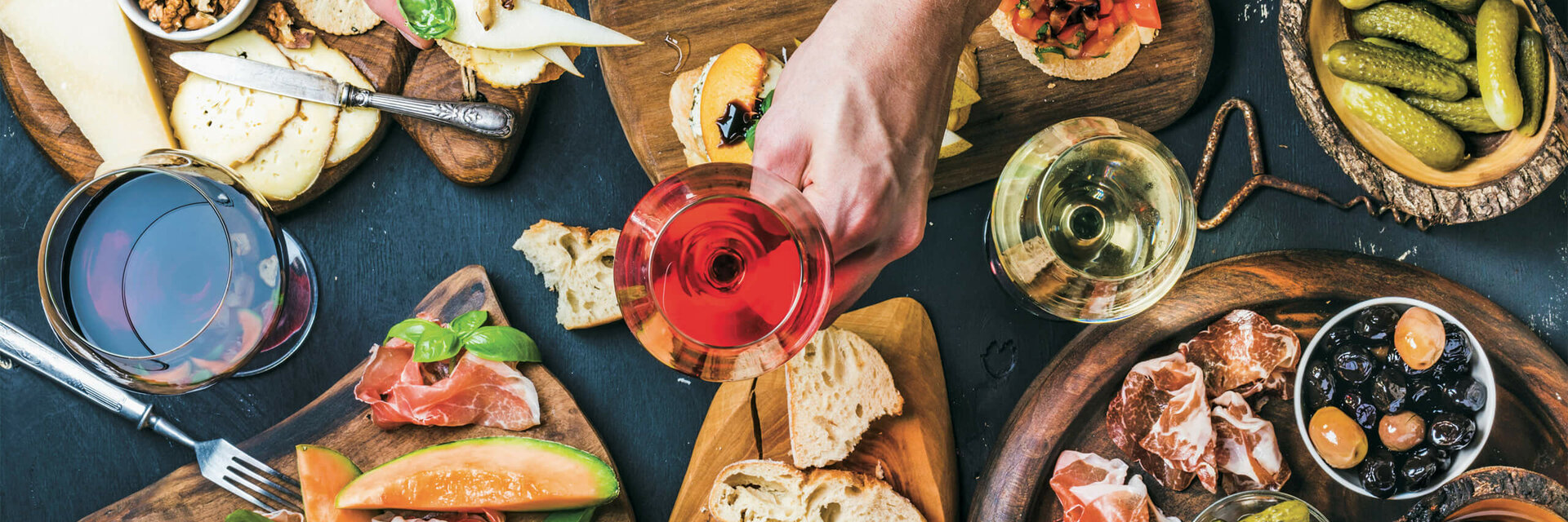 Mediterranean dinner at the restaurant DERBY Various tapas with cheese, bread, ham, olives and wine glasses on wooden boards.