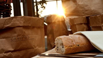 Fresh ingridients and delicious recipees - let us spoil you in our restaurant CAMPUS Loaf of bread and paper bags in the sunlight on a table in the ATLANTIC Hotel Universum Bremen.