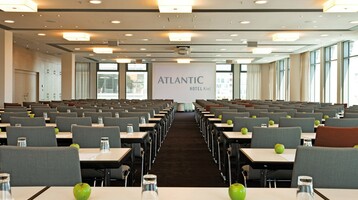 Moderner Konferenzraum mit Reihen grauer Stühle, Tischen mit Gläsern und grünen Äpfeln, große Fenster im Hintergrund.