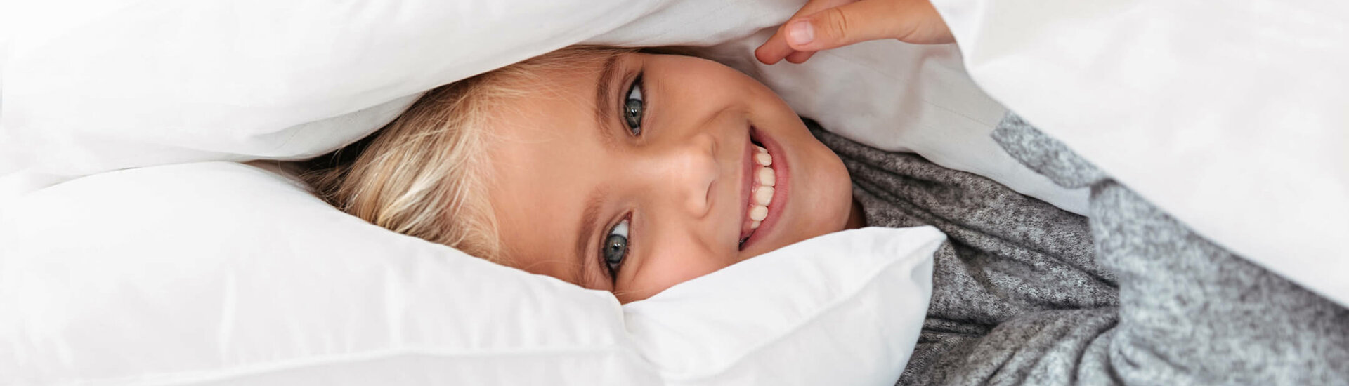 ATLANTIC Hotels 404 Page Hero Smiling child cuddling under white comforters, conveying a sense of security and comfort.