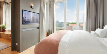 Bedroom of the Balcony Suite at Atlantic Grand Hotel Bremen Bright hotel room with large bed, TV and floor-to-ceiling windows with a view of the city at the ATLANTIC Grand Hotel Bremen.