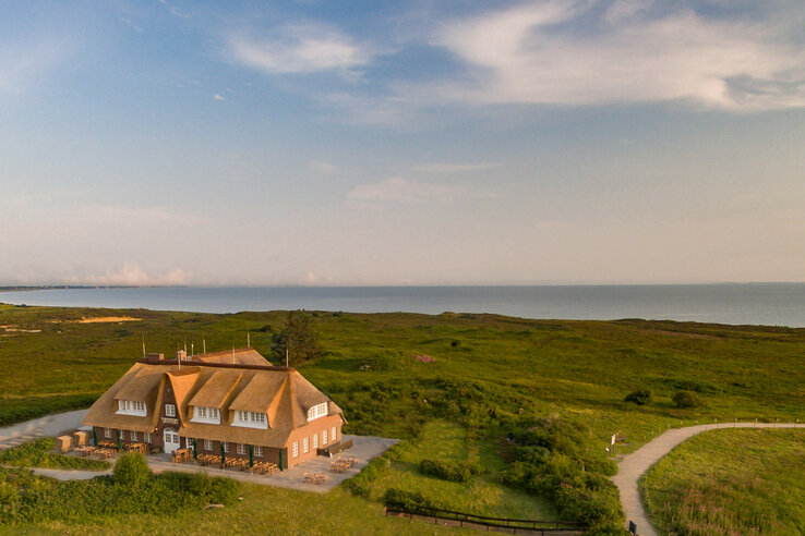Luftaufnahme Landhaus Severin*s Reetgedecktes Hotel Landhaus Severin*s auf Sylt, umgeben von grüner Landschaft, mit Blick auf das Meer.