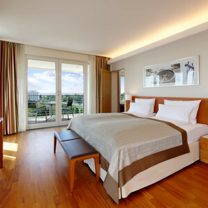 Executive Juniorsuite in the ATLANTIC Hotel Wilhelmshaven Bright hotel room with double bed, wooden floor, TV, balcony with chairs and a wide view of the green landscape.