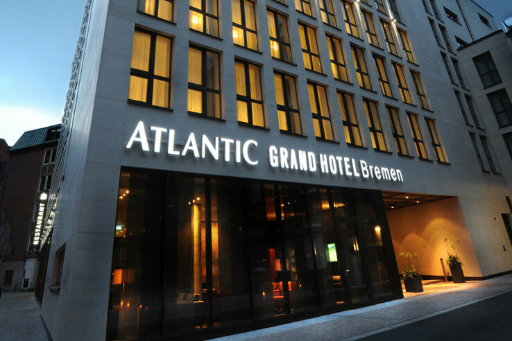 ATLANTIC Grand Hotel Bremen – Außenansicht Fassade des ATLANTIC Grand Hotel Bremen bei Dämmerung, beleuchtetes Logo und moderne Architektur.