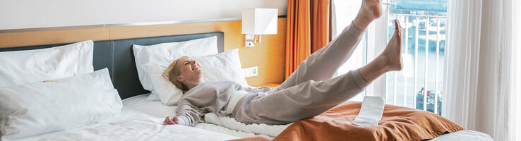 Foto einer Frau im Schlafanzug, die sich rücklings auf ihr Bett fallen lässt.