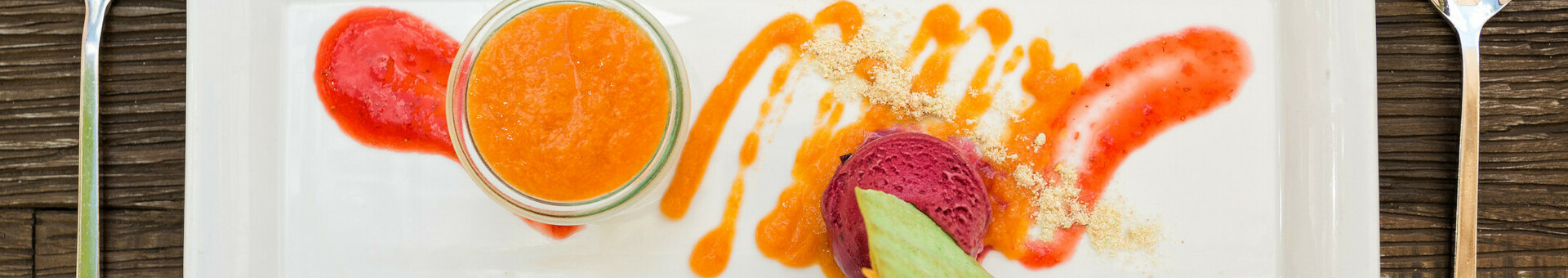 Dessert variation Elegant dessert on a rectangular plate with fruit puree, sorbet and garnish, served on a wooden table.