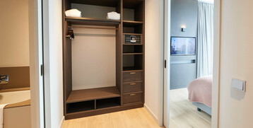 Balcony Suite dressing room at the Atlantic Grand Hotel Bremen Modern hotel room hallway with open closet, safe, bathroom on the left and view into the bedroom with TV.