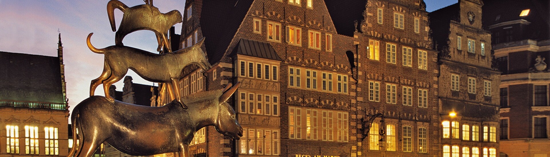 The market place in Bremen with the statue of the Town musicians of Bremen Bronze statue of the Bremen Town Musicians in front of historic buildings in the evening light.