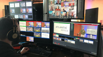Technik Setup Hybride Veranstaltung | ATLANTIC Hotels Person steuert Videokonferenz mit mehreren Bildschirmen, "Atlantic Hotels" Logo sichtbar.