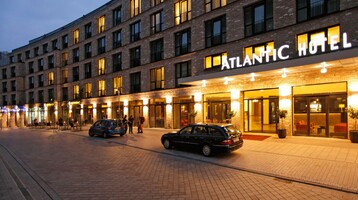 Exterior view of the ATLANTIC Hotel Lübeck while it starts to get dark Exterior view of the ATLANTIC Hotel Lübeck at dusk, illuminated entrance area, parked cars in front of the hotel.