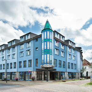 ATLANTIC Hotel Vegesack Bremen Blaues Gebäude des ATLANTIC Hotel Vegesack mit markantem Turm und Eingang, umgeben von Bäumen und Pflasterstraße.