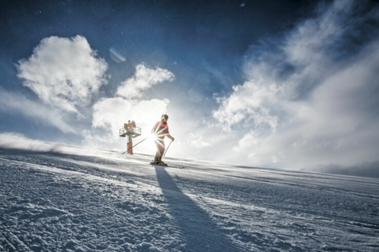 Skiing at Lech am Arlberg / St. Anton Skiers on a sunny, snow-covered slope with a blue sky and clouds in the background.