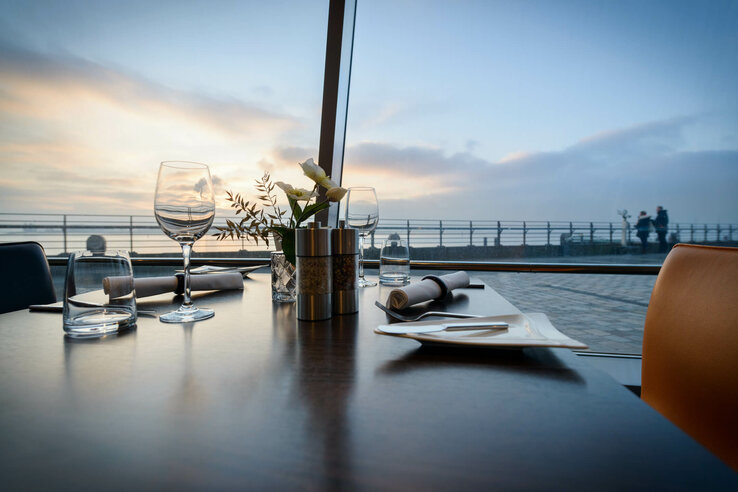 Enjoy high-quality food in our rwstaurant STROM with a panoramic view over the Weser Elegant table setting at the ATLANTIC Hotel Sail City, Bremerhaven, with a view of the promenade at sunset.