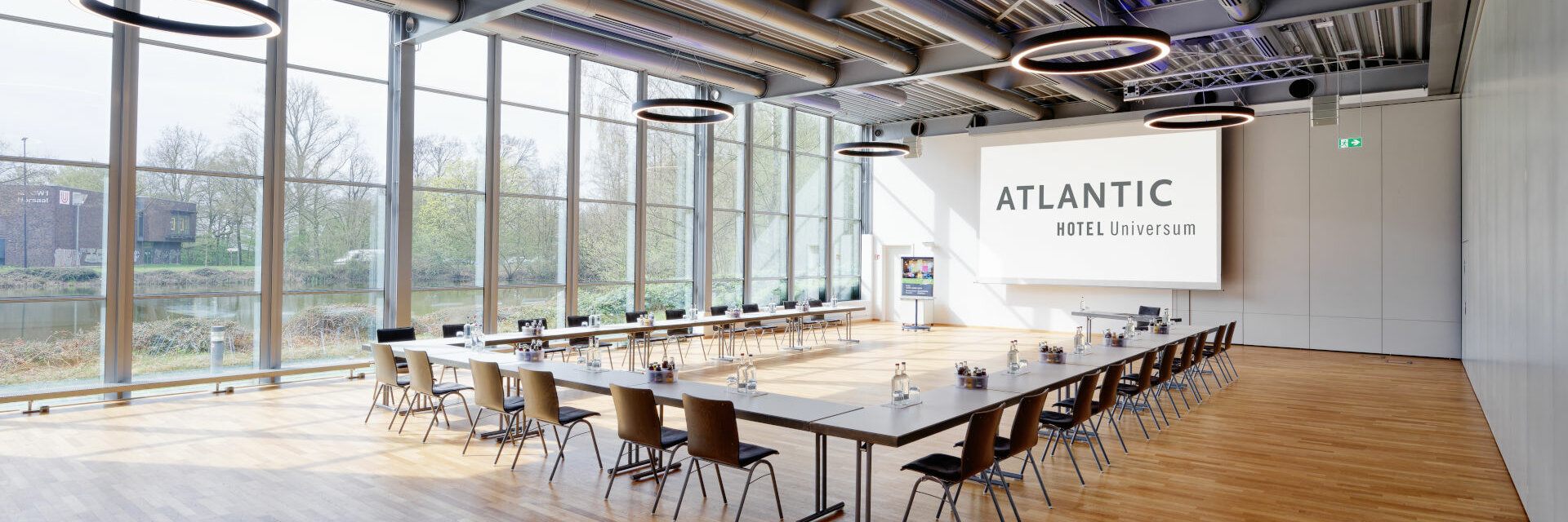 Modern conference room in the ATLANTIC Hotel Universum with large windows, U-shaped table arrangement and screen.