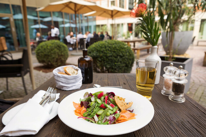 Summery salad with asparagus and salmon in the Hofgarten of the ATLANTIC Grand Hotel Bremen Salad with salmon on a wooden table at the ATLANTIC Grand Hotel Bremen, terrace with guests in the background.