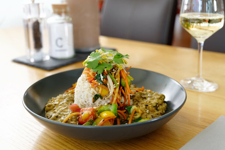 eat in the ATLANTIC Hotel Bremen Universum Colorful curry dish with rice and vegetables, decorated with herbs, on a wooden table at the ATLANTIC Hotel Universum, Bremen.