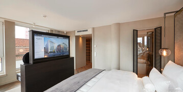 Bedroom in the Grand Suite at the Atlantic Grand Hotel Bremen Modern hotel room with large bed, flat-screen TV, stylish lighting and view of a terrace.