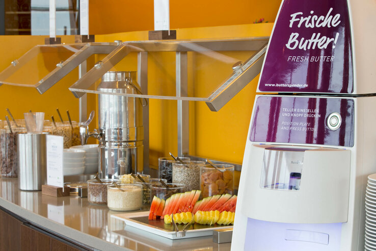 Breakfast area in the ATLANTIC Hotel Sail City Bremerhaven Breakfast buffet with cereals, fruit, butter dispenser and dishes at the ATLANTIC Hotel Sail City, Bremerhaven.