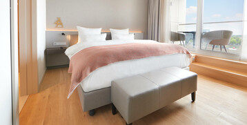 Sleeping area of the Executive Suite in the ATLANTIC Grand Hotel Bremen Modern hotel room with double bed, light wooden floor and balcony with a view of the city at the ATLANTIC Grand Hotel Bremen.