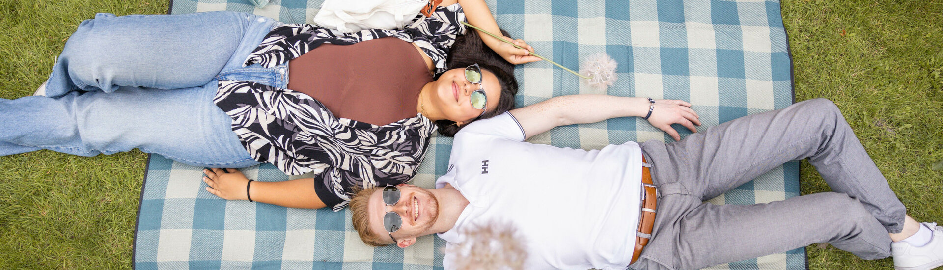 Freizeit im Grünen genießen im ATLANTIC Hotel Landgut Horn A couple lies smiling on a blue plaid picnic blanket