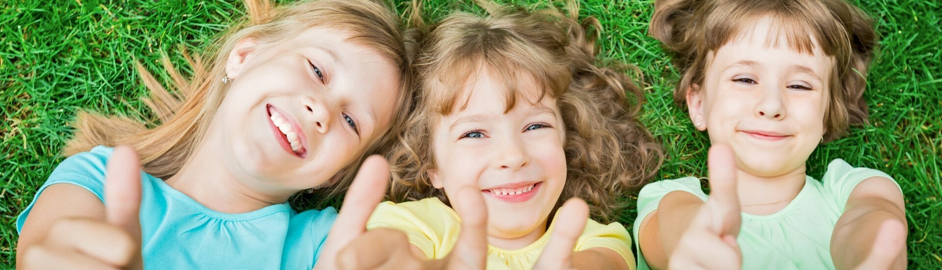 Kids on a meadow in front of the ATLANTIC Hotel Universum Bremen Three laughing children lie on the grass and give the thumbs up.
