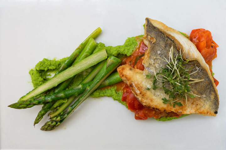 Dinner is served in the ATLANTIC Grand Hotel Bremen Fried fish with asparagus, pea puree and tomatoes on a white plate, at the ATLANTIC Grand Hotel Bremen.