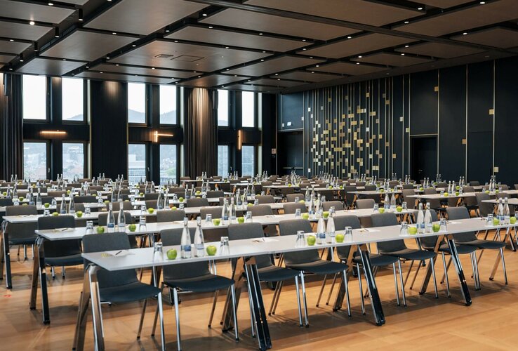 ATLANTIC Hotel Heidelberg Ballsaal mit parlamentarischer Bestuhlung Moderner Konferenzraum im ATLANTIC Hotel Heidelberg mit Reihen von Tischen und Stühlen, großen Fenstern und eleganter Beleuchtung.