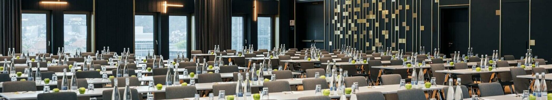 ATLANTIC Hotel Heidelberg Ballsaal mit parlamentarischer Bestuhlung Moderner Konferenzraum im ATLANTIC Hotel Heidelberg mit Reihen von Tischen und Stühlen, großen Fenstern und eleganter Beleuchtung.