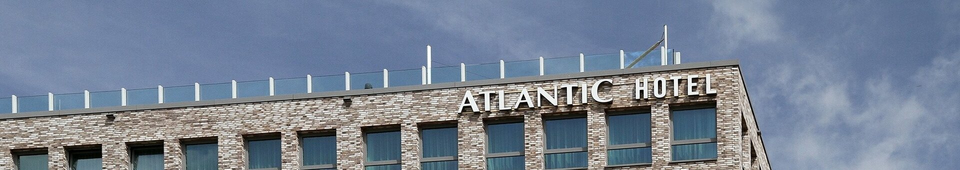 Exterior view of the ATLANTIC Hotel Kiel Modern brick hotel façade with many windows and balconies, blue sky in the background.