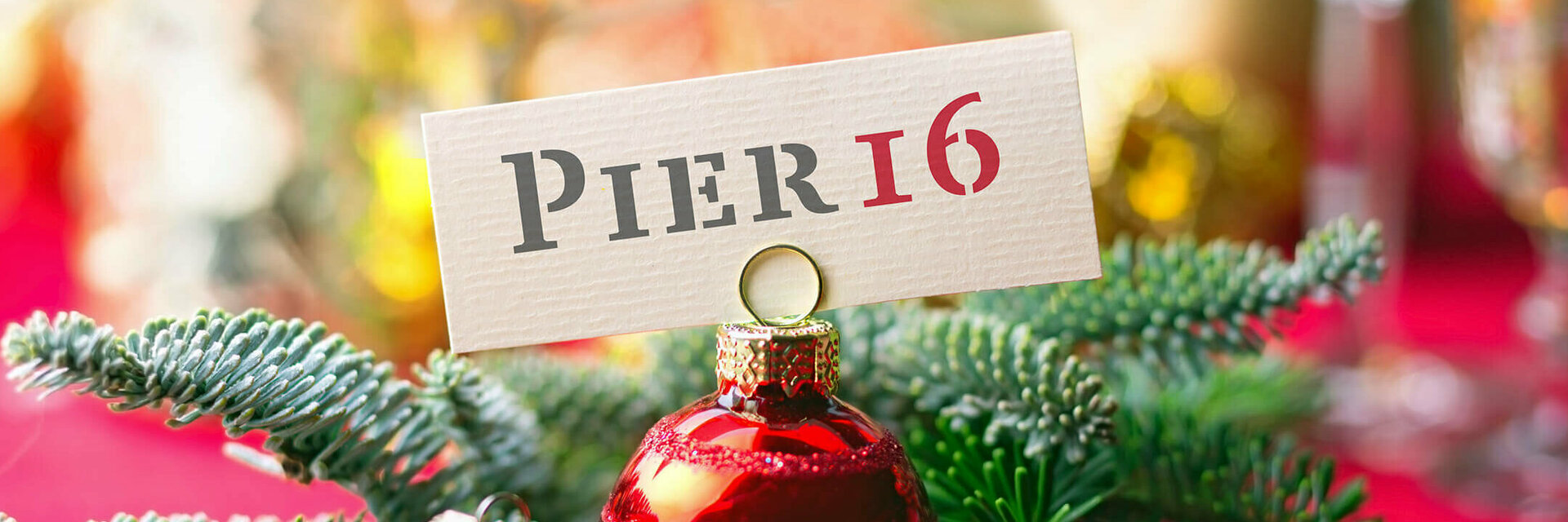 ATLANTIC Hotel Kiel Weihnachtsfrühstück Weihnachtlicher Tannenzweig und Weihnachtskugel halten ein "PIER16" Schild