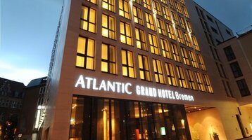 Außenansicht ATLANTIC Grand Hotel in Bremen in der Abenddämmerung Modernes Hotelgebäude bei Dämmerung, mit beleuchteten Fenstern und dem Schriftzug "ATLANTIC Grand Hotel Bremen".