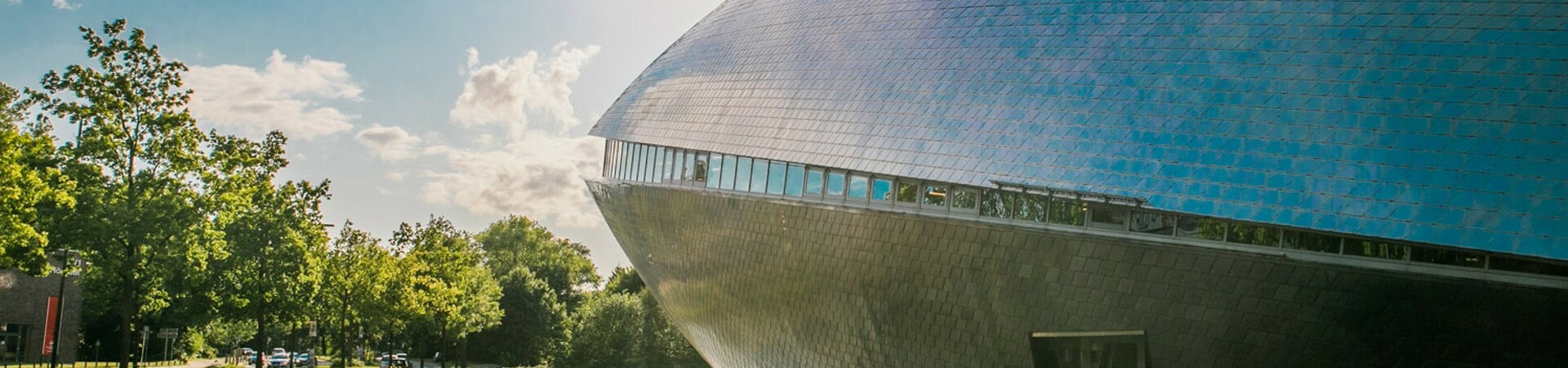 View of the Universum Bremen with the sun in the background Futuristic building with a gleaming façade on the waterfront, surrounded by trees and sunny skies.