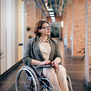 ATLANTIC Hotels Tagen und Feiern für alle Person im Rollstuhl in einem modernen, hellen Korridor mit Pflanzen und Backsteinwänden.