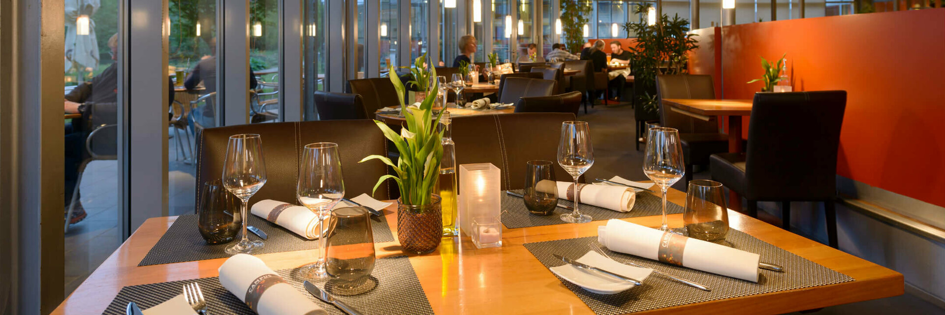 Restaurant CAMPUS des ATLANTIC Hotel Universum in Bremen Modernes Hotelrestaurant mit gedeckten Tischen, großen Fenstern und stimmungsvoller Beleuchtung im ATLANTIC Hotel Universum.