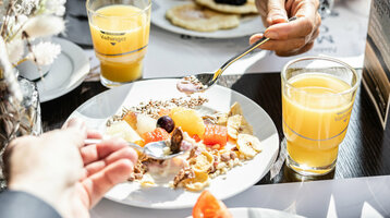 Auf einem gedeckten Frühstückstisch steht ein Birchermüsli und zwei Gläserorangensaft